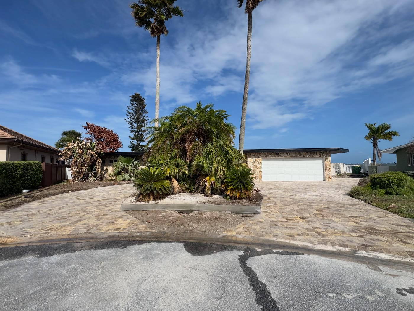 The same waterfront house after: a new paver driveway around a planted island of palms.
