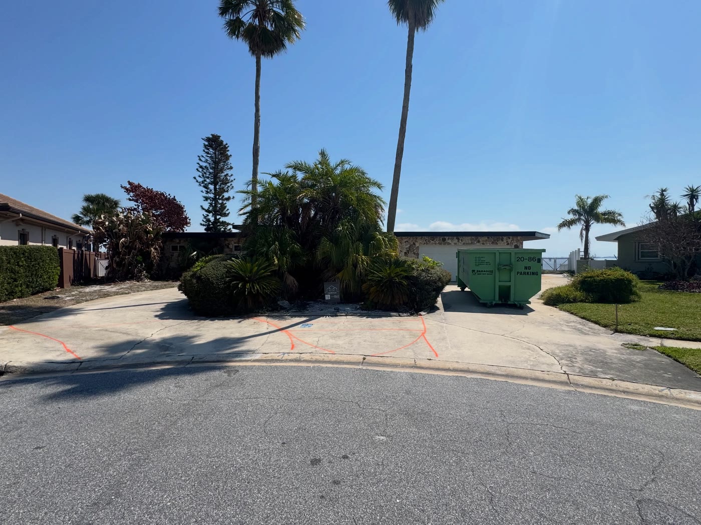 The house before: an old concrete driveway marked out in orange paint, a dumpster at the side.