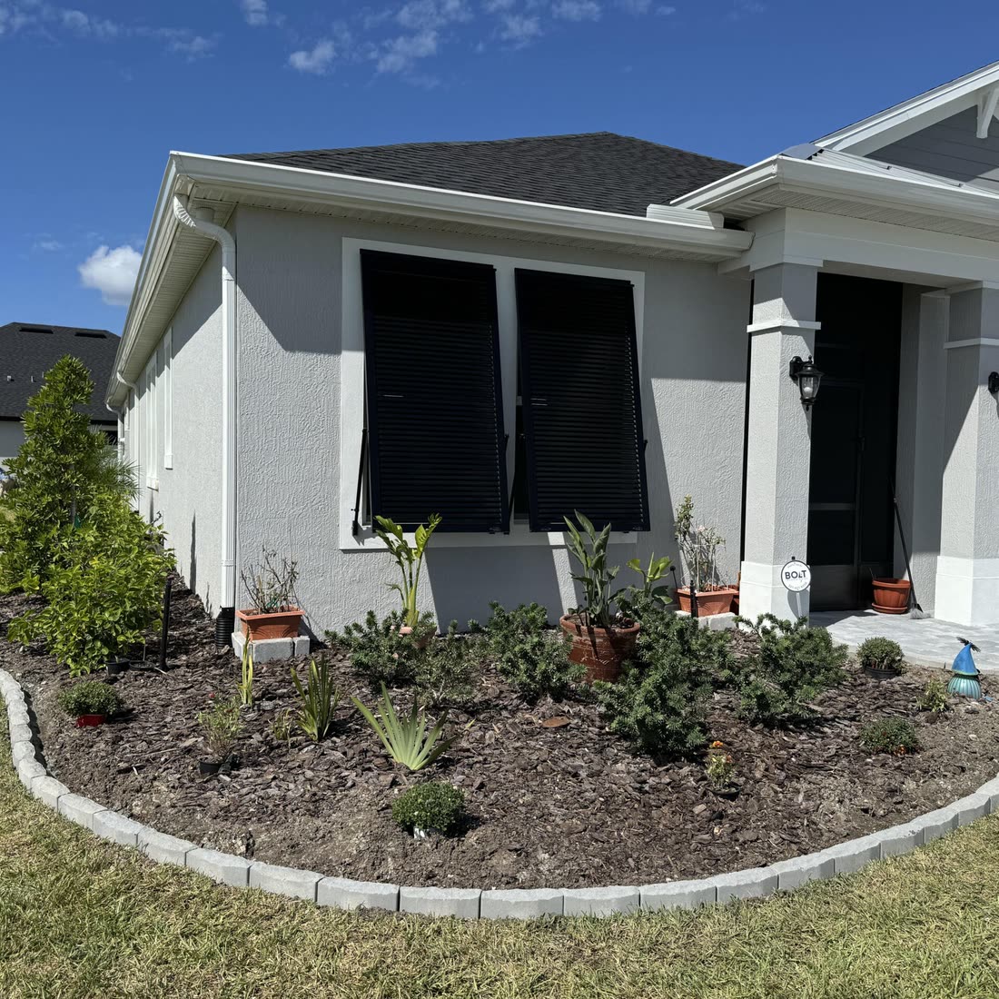 A curved paver border edging a planted front bed in front of a grey house.