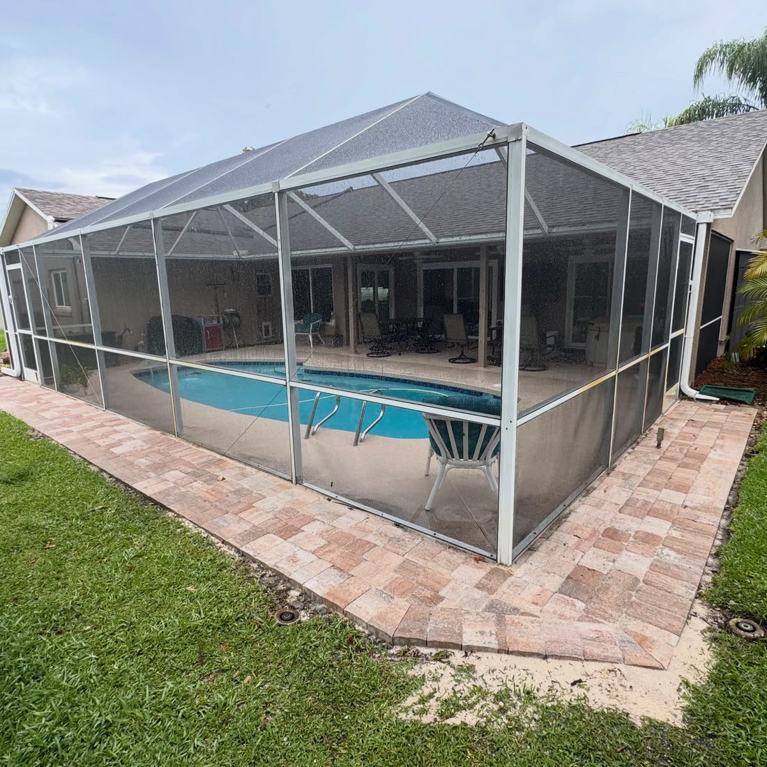 Pavers laid around the outside of a screened pool enclosure, the pool inside.