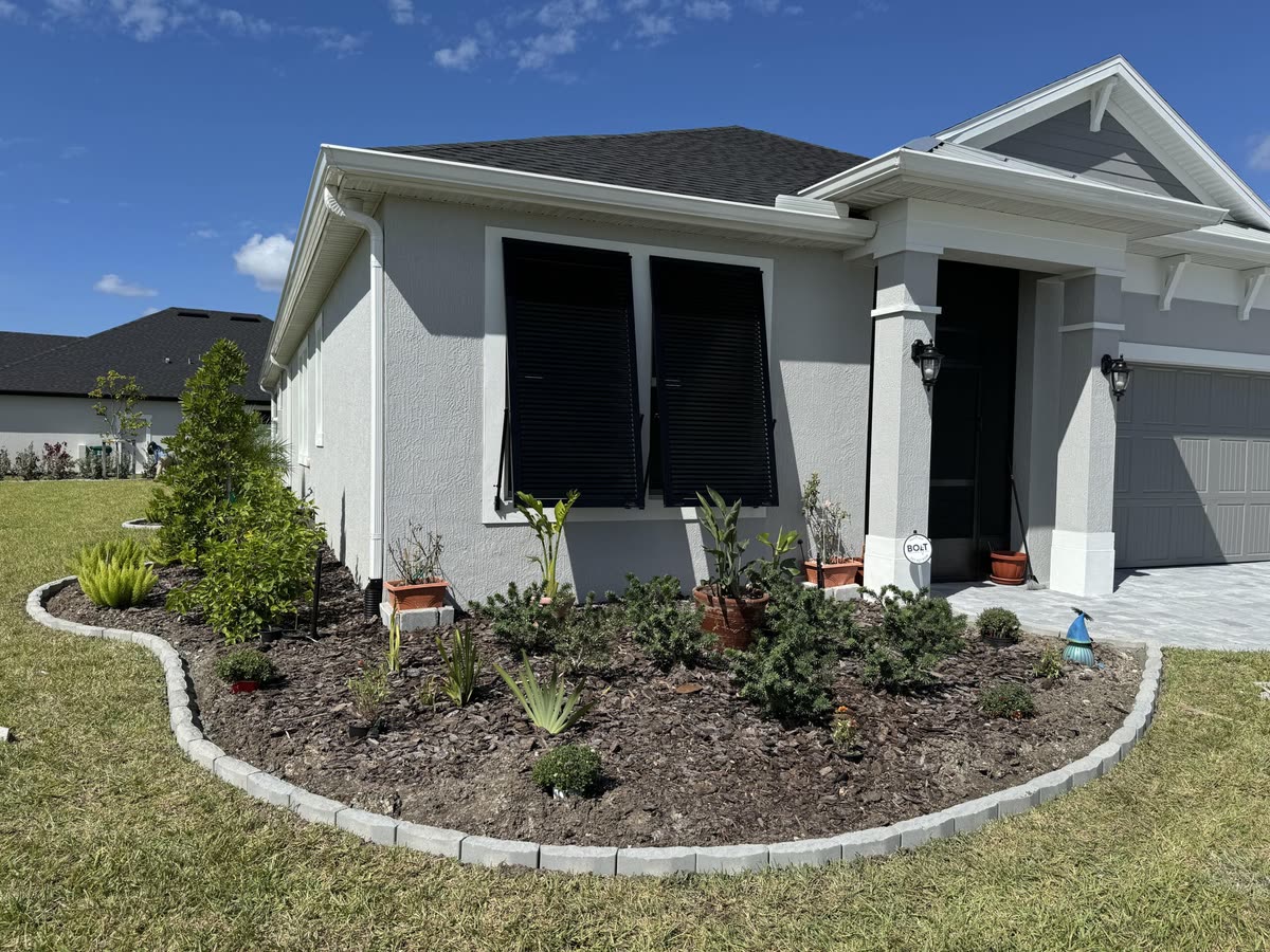 A curved paver border around a planted front bed at a grey house.