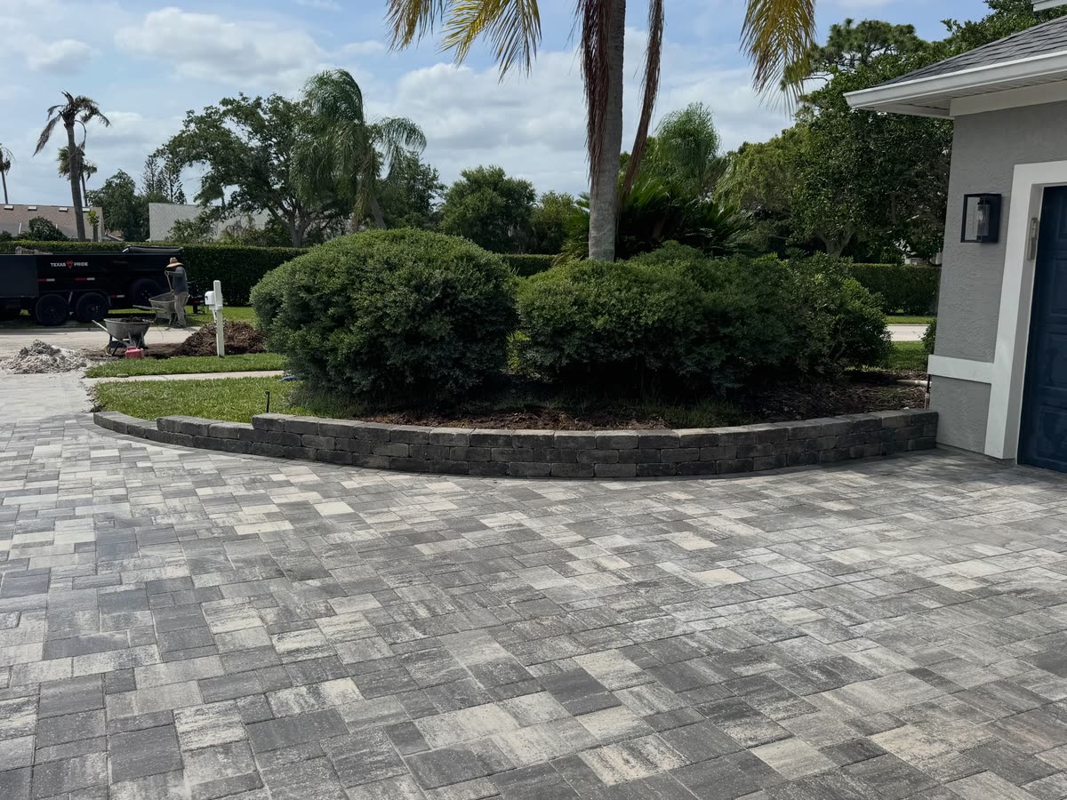 A grey paver driveway sweeping past the corner of a house and around a planted island.