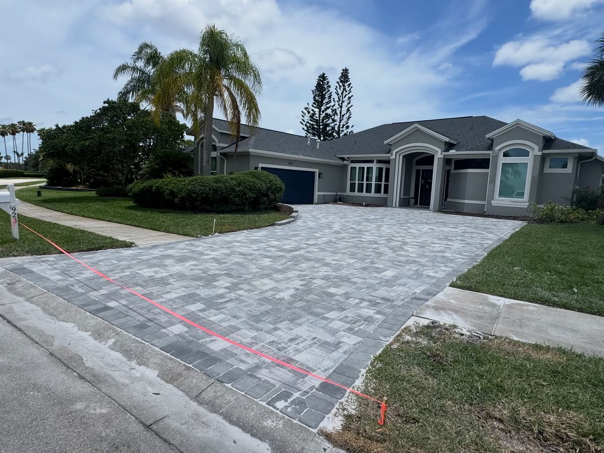 A wide paver driveway in front of a grey house, marking paint still on the edge of the street.