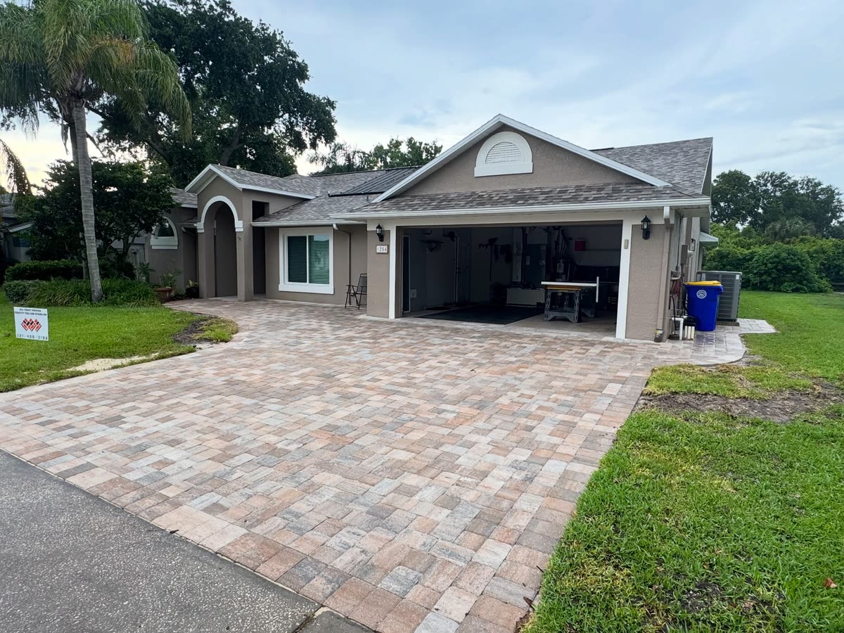 A paver driveway leading to an open double garage at a grey house.