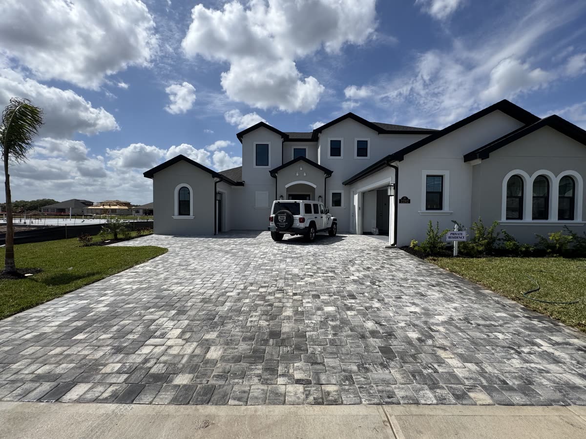 A paver driveway in front of a two-storey house with arched windows, a Jeep parked on it.