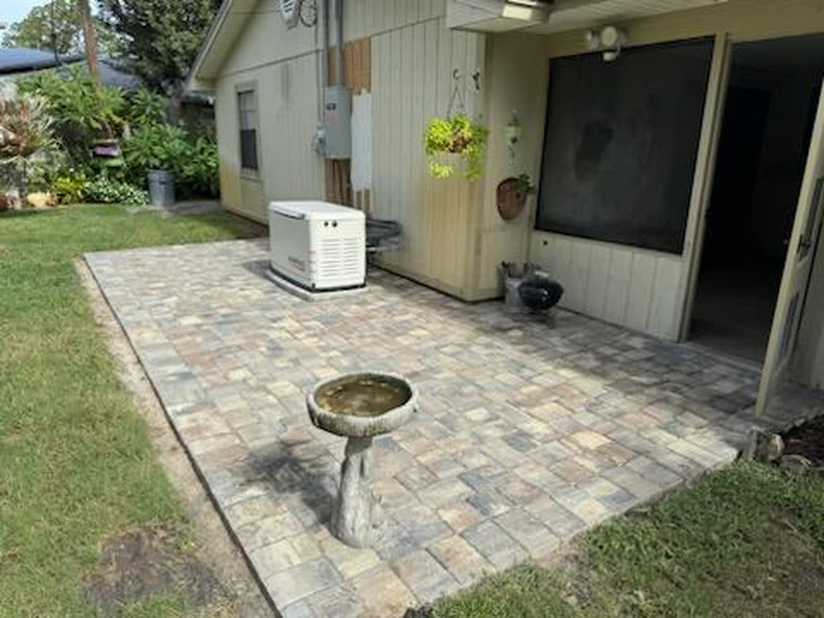 A small paver patio outside a screened porch, with a birdbath on it.