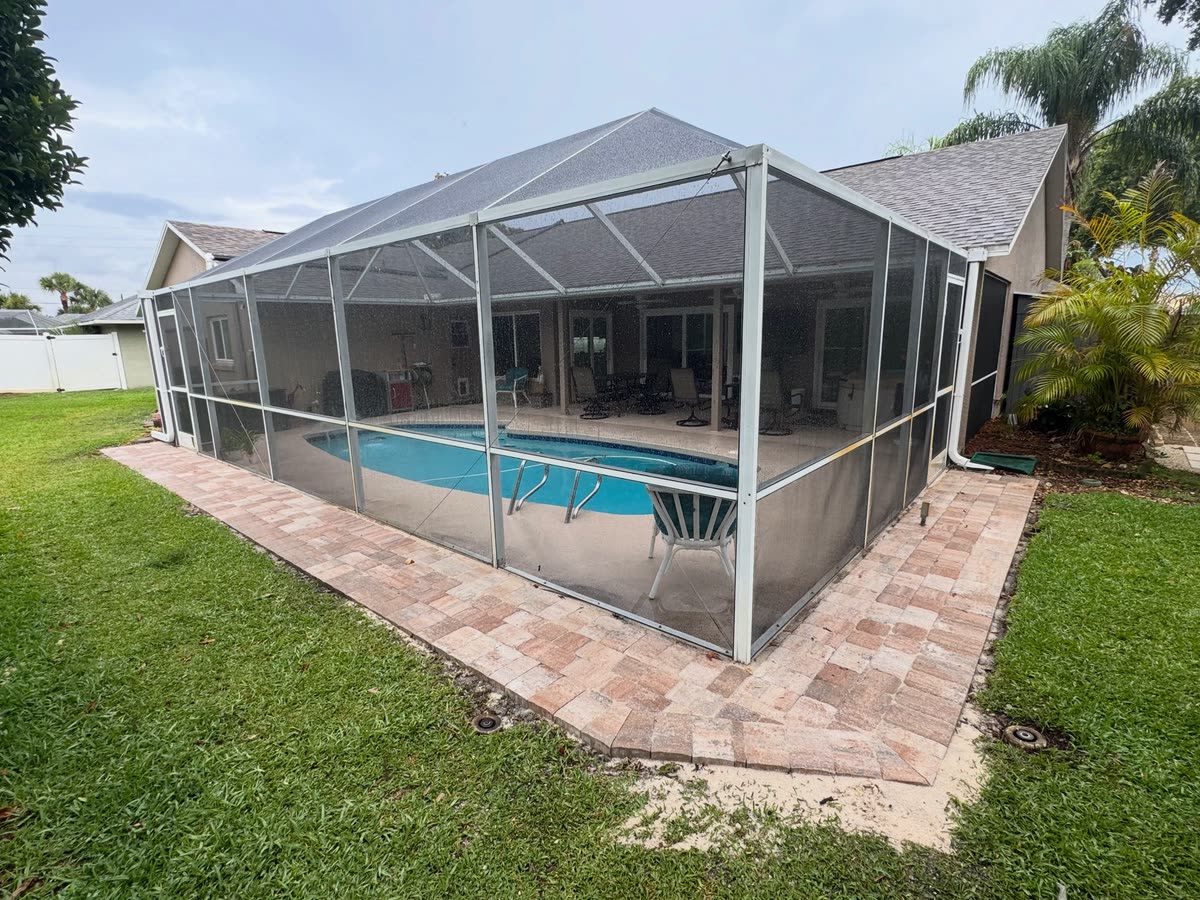 Pavers laid around the outside of a screened pool enclosure, the pool inside.