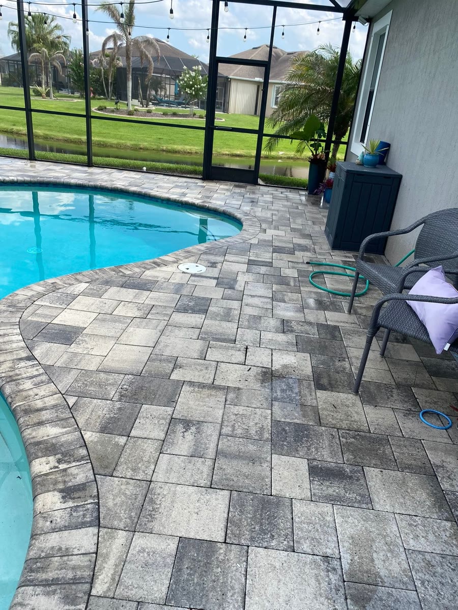 Grey and white pavers curving around a screened pool, chairs on the deck.