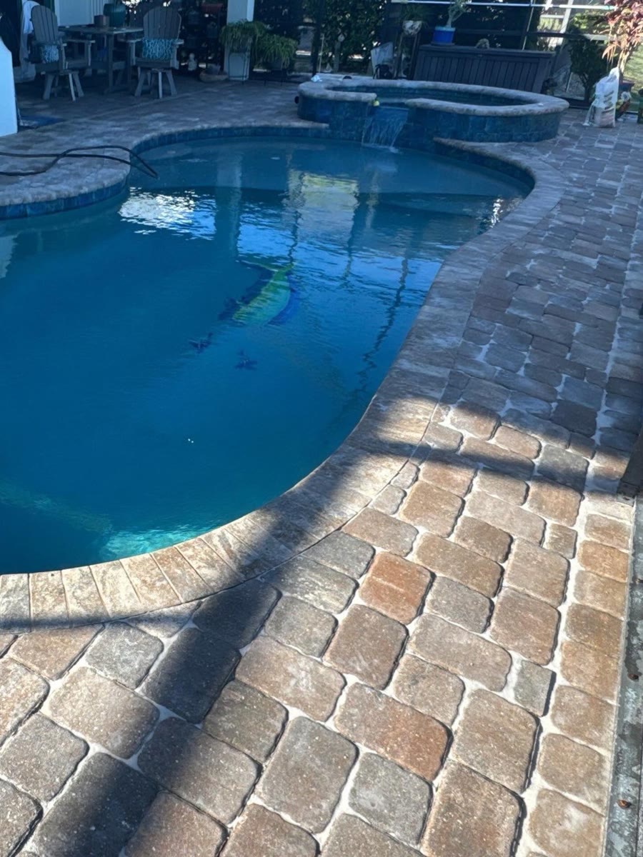 A pool and spa edged in tumbled pavers in rust and tan.