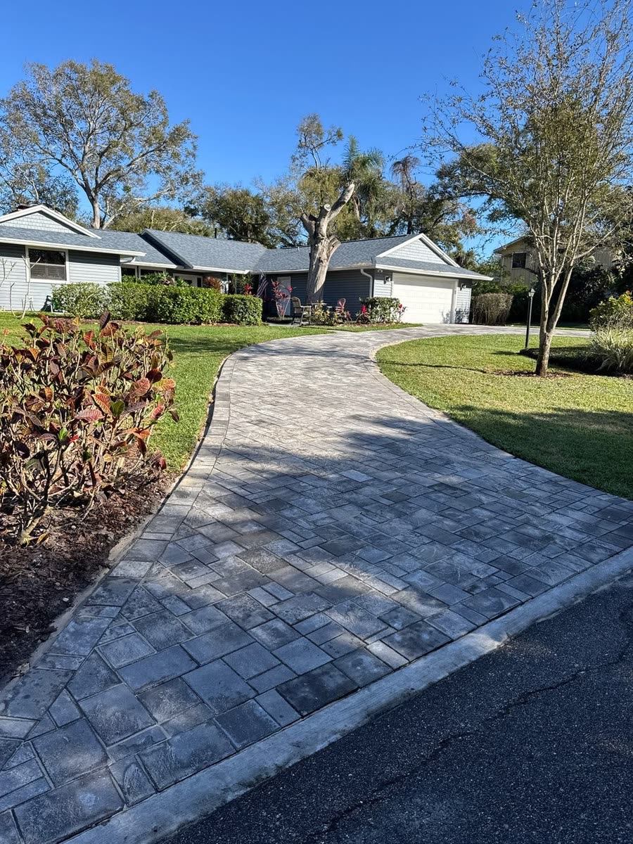 A paver walkway running up from the street past a garden bed.